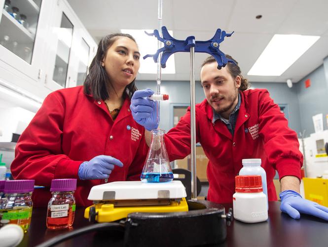 Two researchers in red lab coats working in a laboratory.