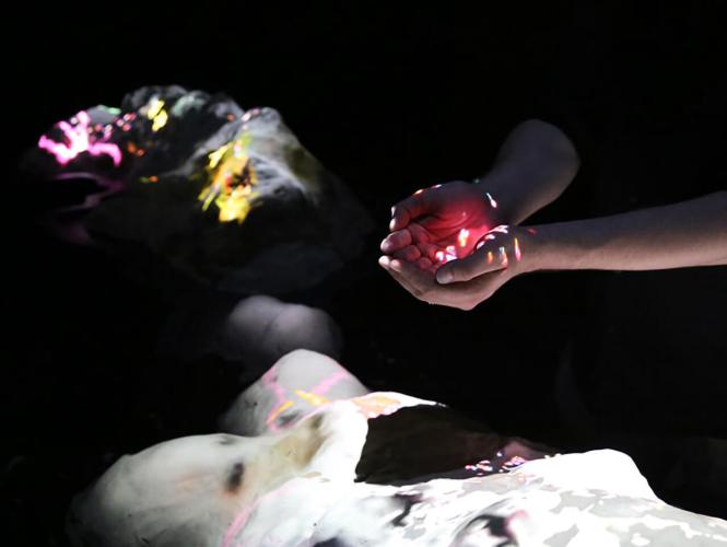 Close-up of a pair of hands hovering over a colorful projection inside a dark room.