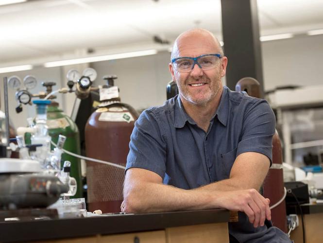 A researcher posing at the end of a table with research equipment on it.