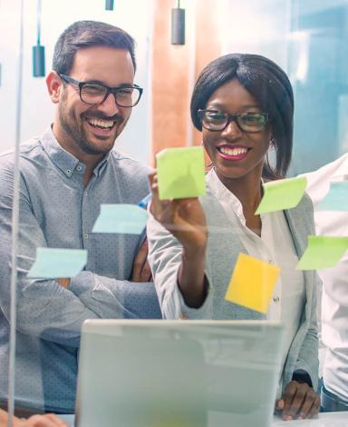 Photo of a group of office employees in front of a glass wall covered in Post-It notes.