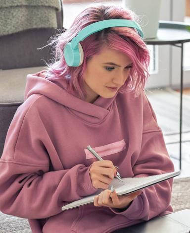 A young person sitting in front of laptop taking notes on a notebook.