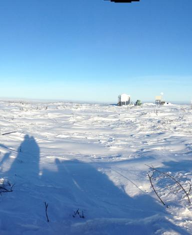 A panorama of a snowy, treeless landscape taken from on top of a snow machine with a meteorological tower and its guy-wires visible.
