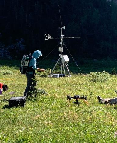 Trois personnes, l’une debout, l’autre accroupie et la troisième allongée dans une zone herbeuse, regardent leurs équipements de recherche : drones, antennes et ordinateurs en tout genre.