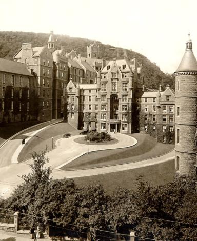 A grey and white photo of a multi-storeyed building with turrets at each corner and a large circular driveway in front.