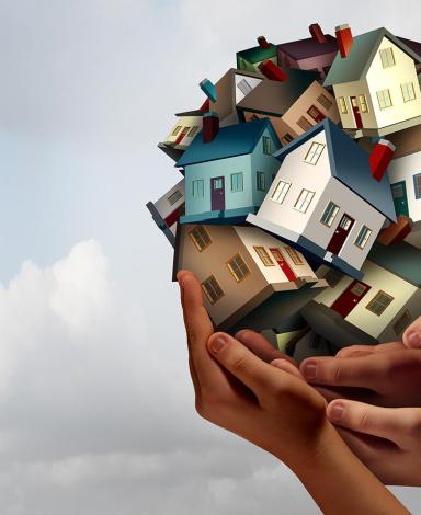 Several hands hold up an illustrated ball of houses against a cloudy sky.