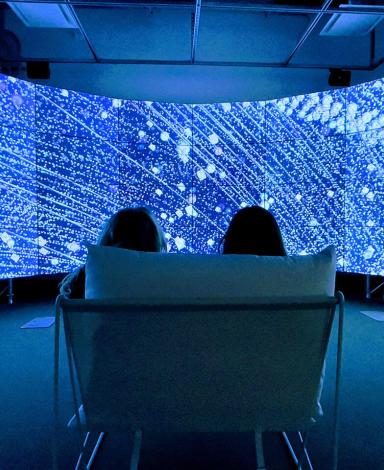Deux personnes sont assises devant un mur vidéo incurvé qui affiche des rendus lumineux de satellites en orbite autour de la Terre.
