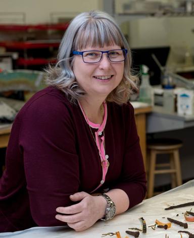 Lisa Rankin est appuyée sur un comptoir de laboratoire jonché d’artefacts archéologiques.