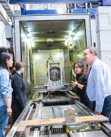 A group of people stand on either side of a long metal machine.