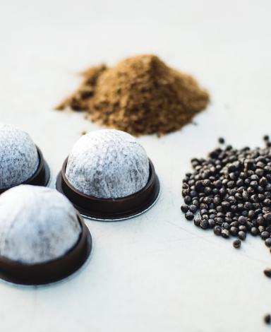 Trois petits tas de grains de café, de marc de café et de dosettes de café sur un fond blanc
