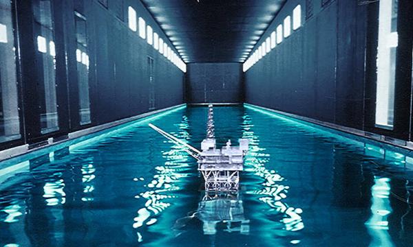 An elongated pool of water enclosed between solid walls with a model of an oil rig in the middle of the water.