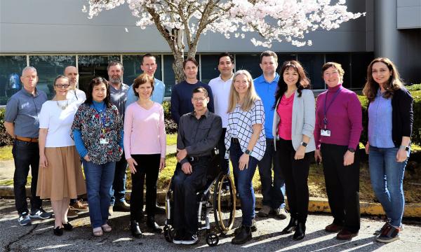 A man sitting in a wheelchair is surrounded by a group of people under a flowering tree.