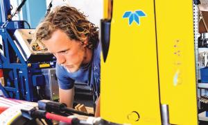 Une personne se penche pour regarder de près un appareil cylindrique sur une surface de travail dans un laboratoire.