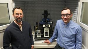 Two people stand in front of a microscope.