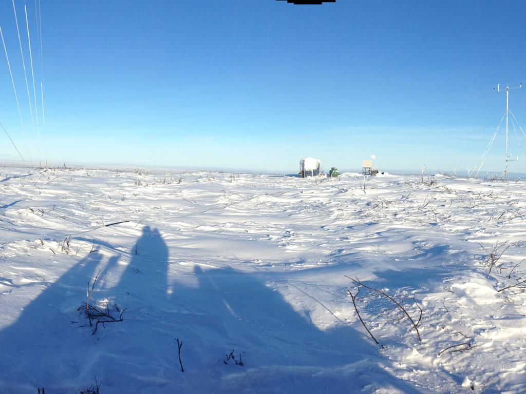 A panorama of a snowy, treeless landscape taken from on top of a snow machine with a meteorological tower and its guy-wires visible.