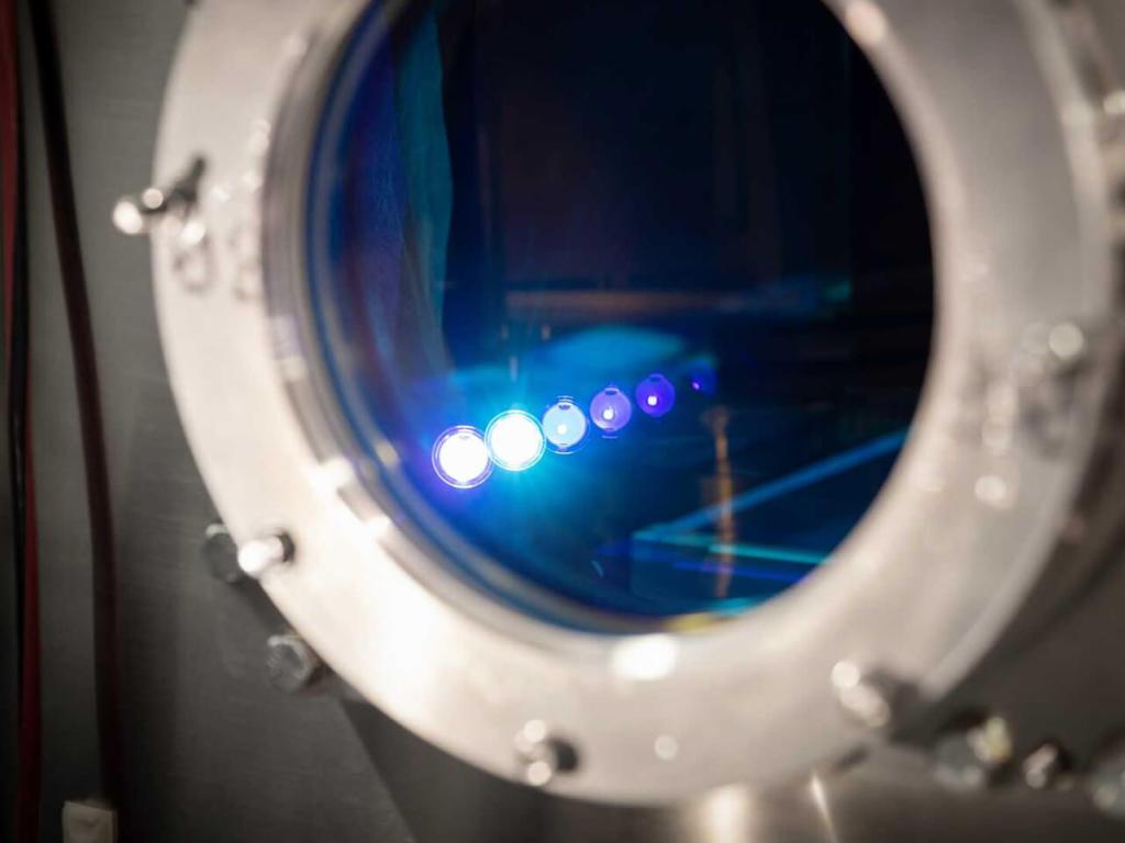 A close-up view of a vacuum chamber with several points of light in focus inside a circular window.