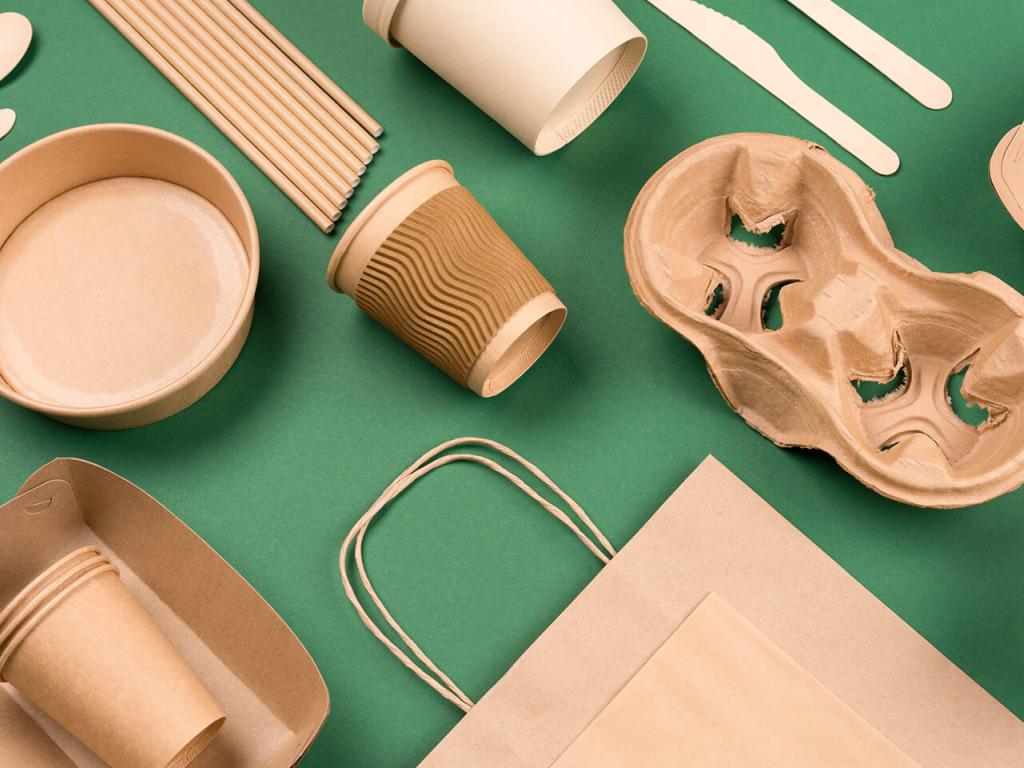 Gobelets, couverts et plateaux en carton ainsi que sacs en papier brun disposés de manière ordonnée sur un fond vert.