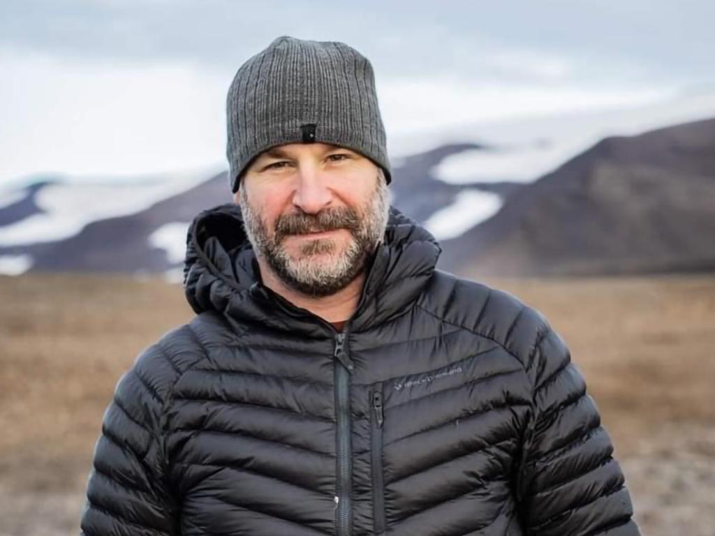 A person wearing a coat in an empty field, posing for a photo.