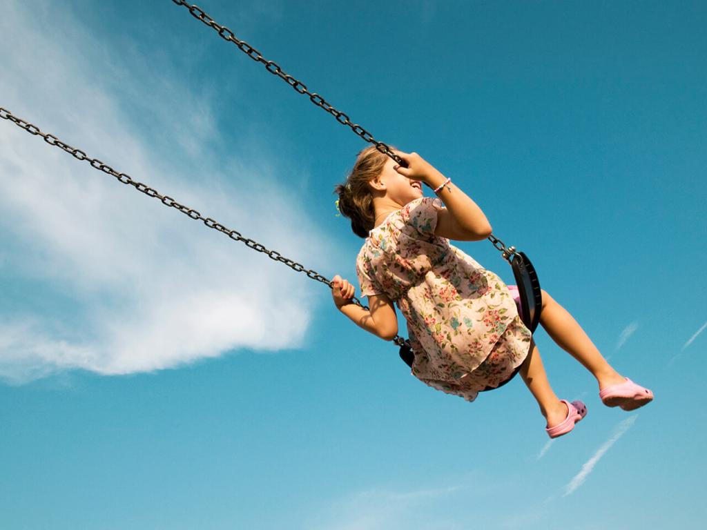 A child on a swing against a blue sky.