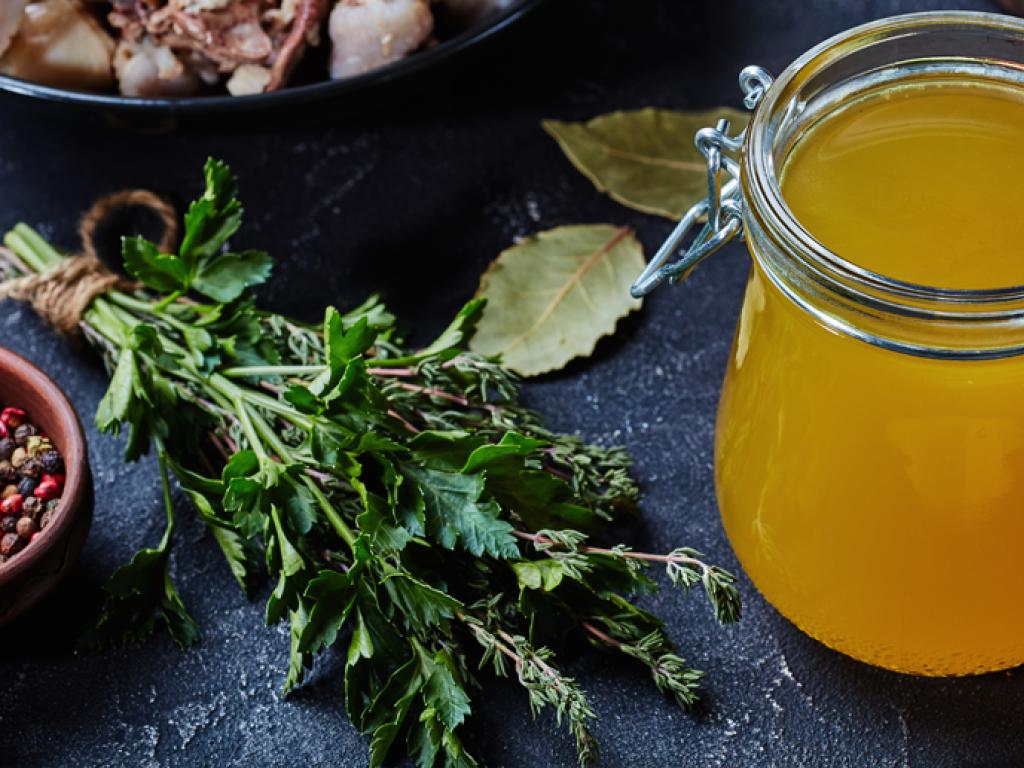 Un bocal de liquide jaune avec à côté, des herbes fraîches et un bol de grains de poivre