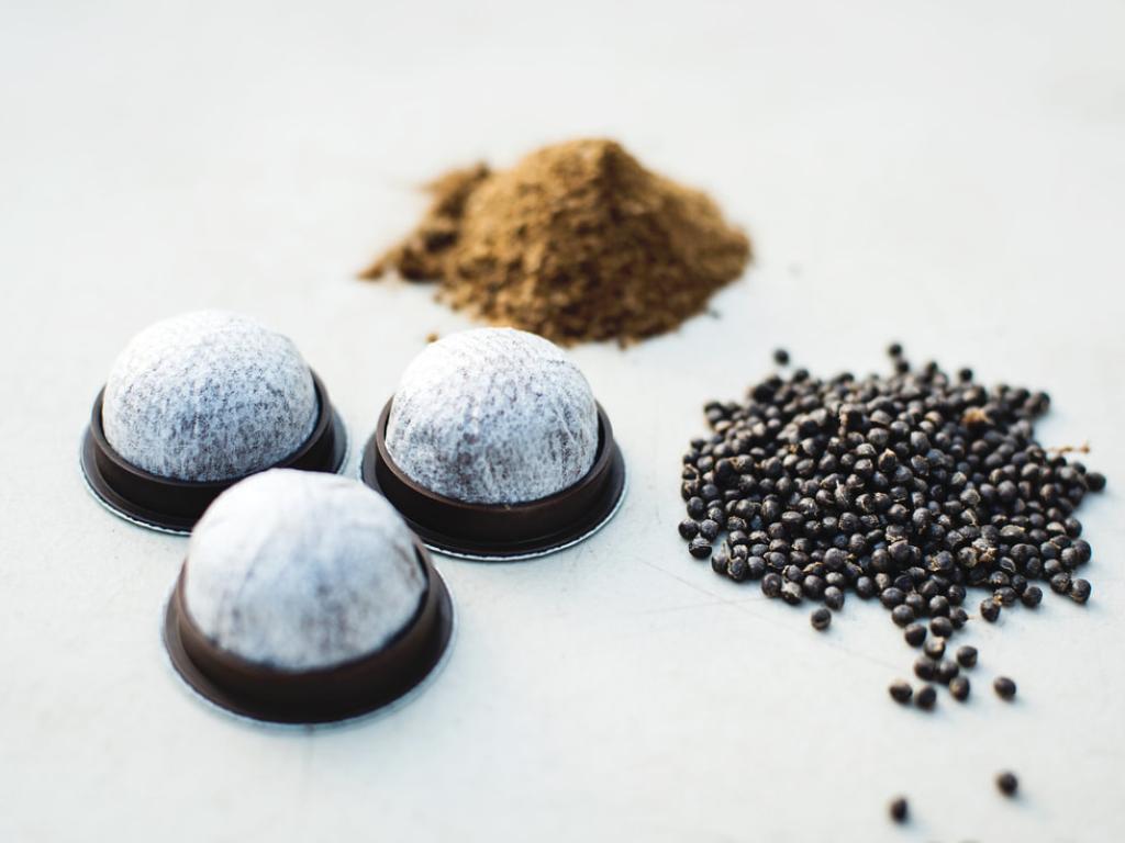 Three small piles of coffee beans, coffee grounds and coffee pods on a white background
