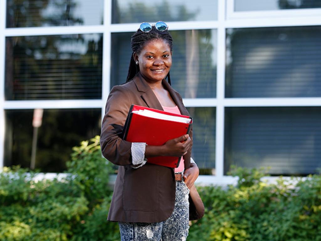 Jacqueline Mboko, an interpreter for London's Cross Cultural Learner Centre, holding a red binder posing for a photo outside.