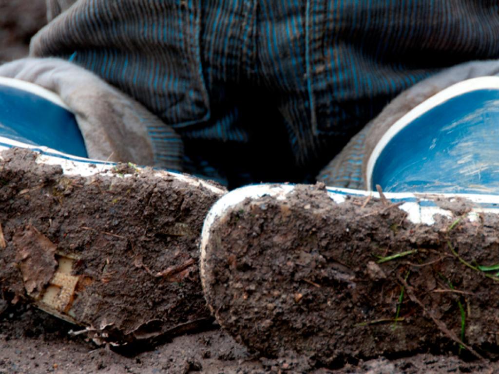 The soles of a child’s blue rubber boots, caked in mud