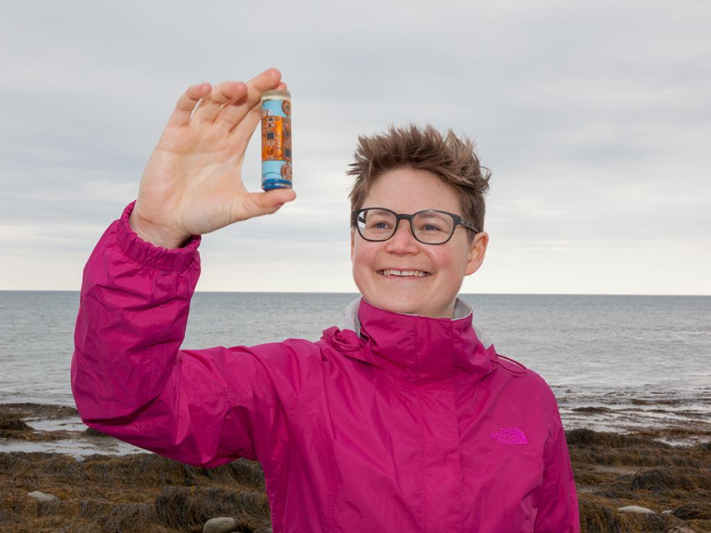 Dr. Franziska Broell holding a small container in front of an ocean view.