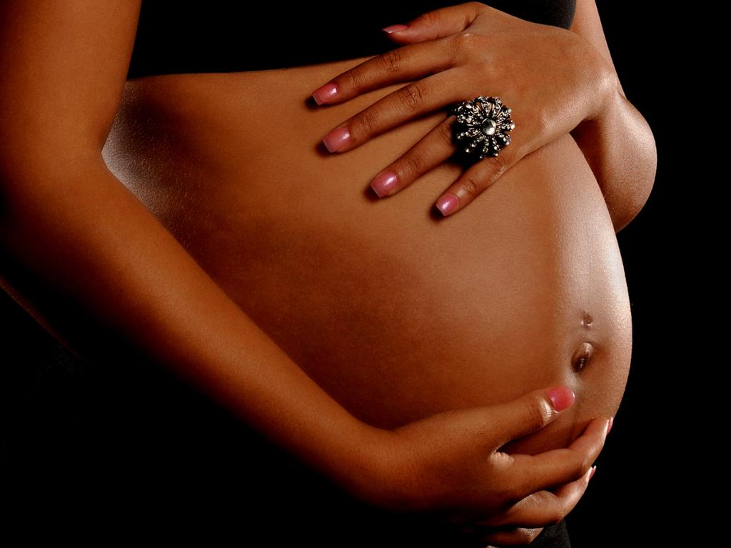 A close up shot of a woman’s hands on her pregnant stomach. 