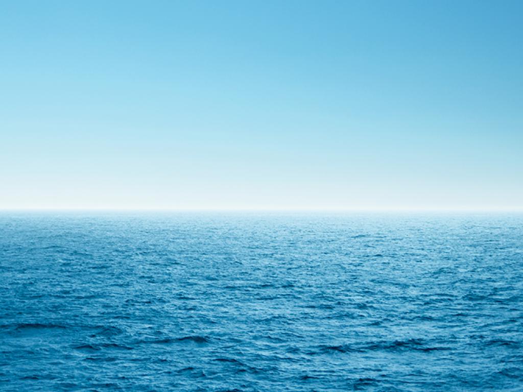 A thin white line on the horizon separates a wide expanse of blue ocean from a blue sky