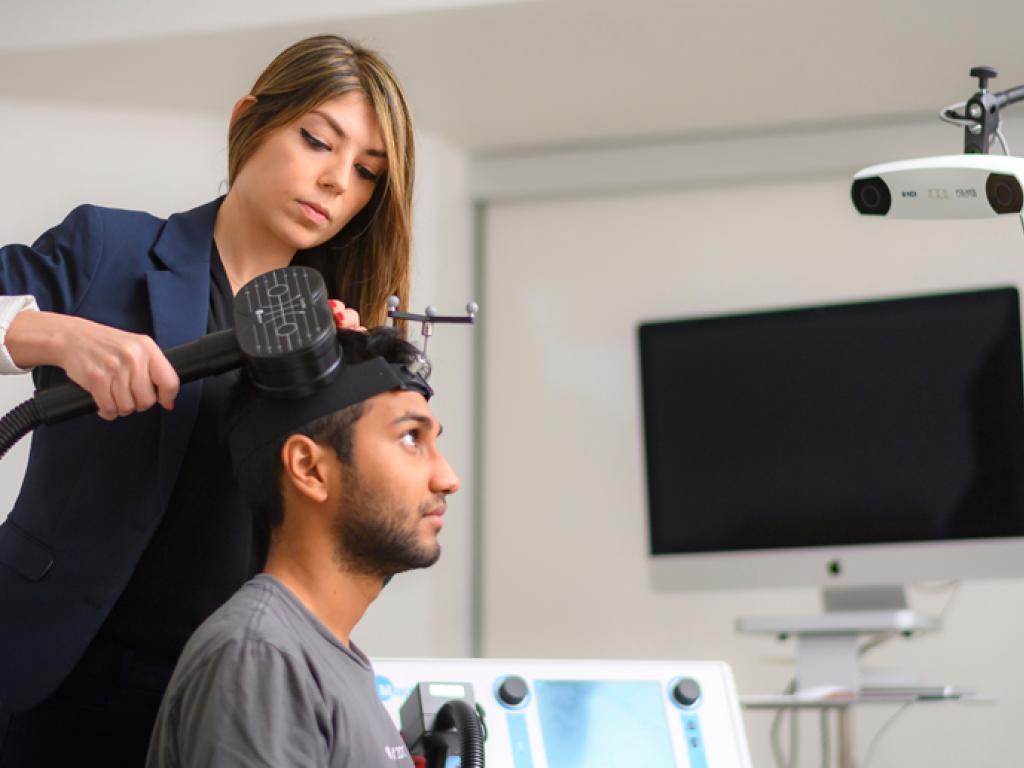 Faranak Farzan applies a device to the side of a seated man’s head