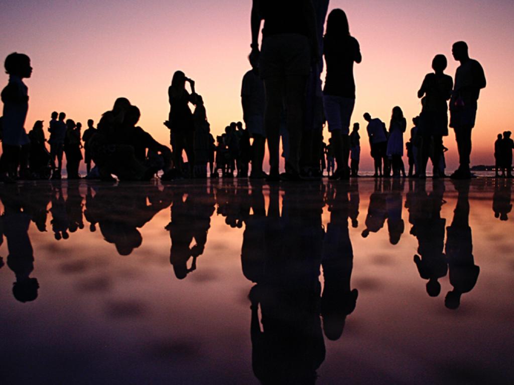 Silhouettes de nombreuses personnes en interaction sur une surface réflectrice qui ressemble à de l’eau.