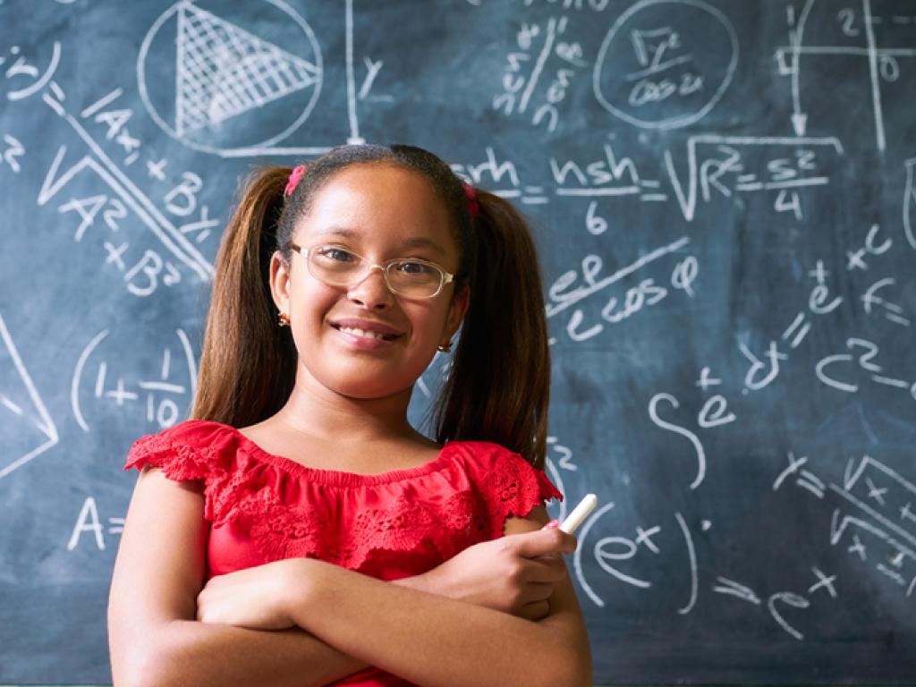 Pigtailed girl stands in front of chalkboard containing many mathematical