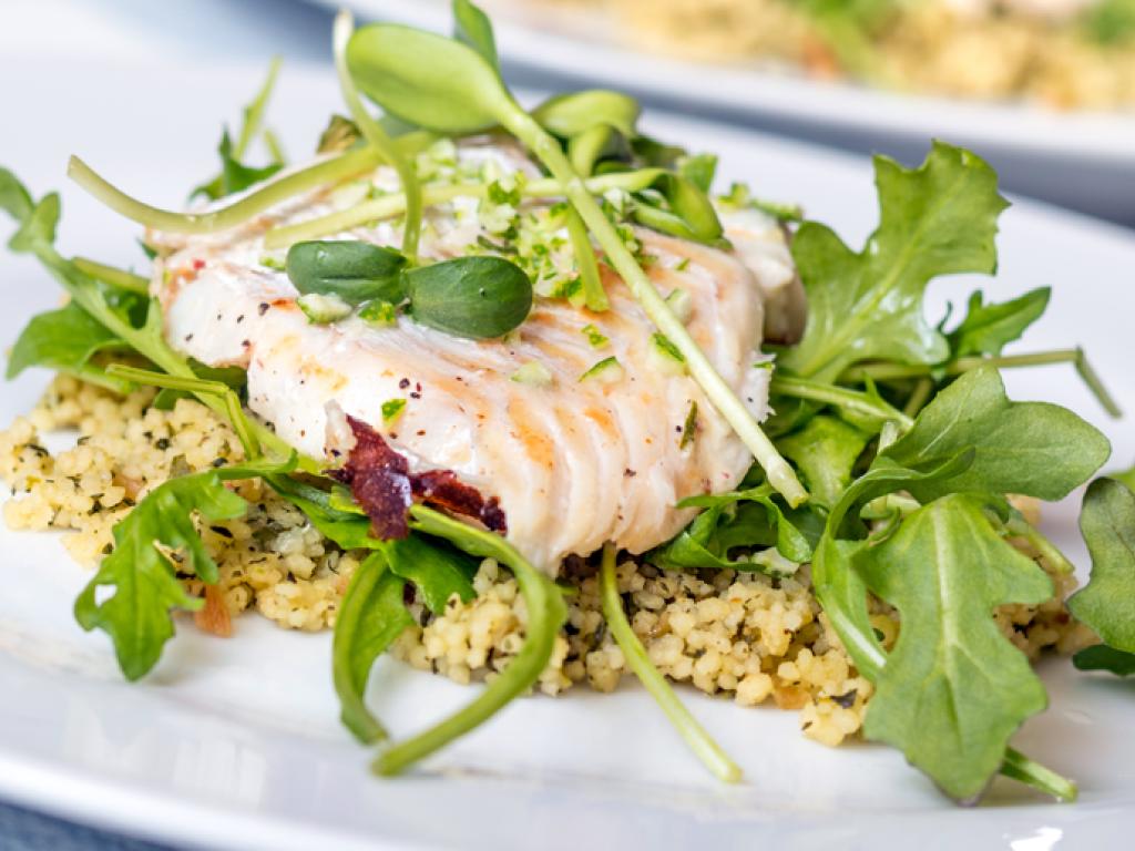 Une assiette de filet de bar cuit sur un lit de roquette et couscous