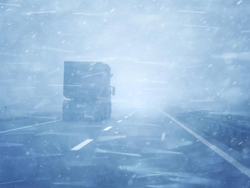 A transport truck on a snow-covered road in a blizzard.