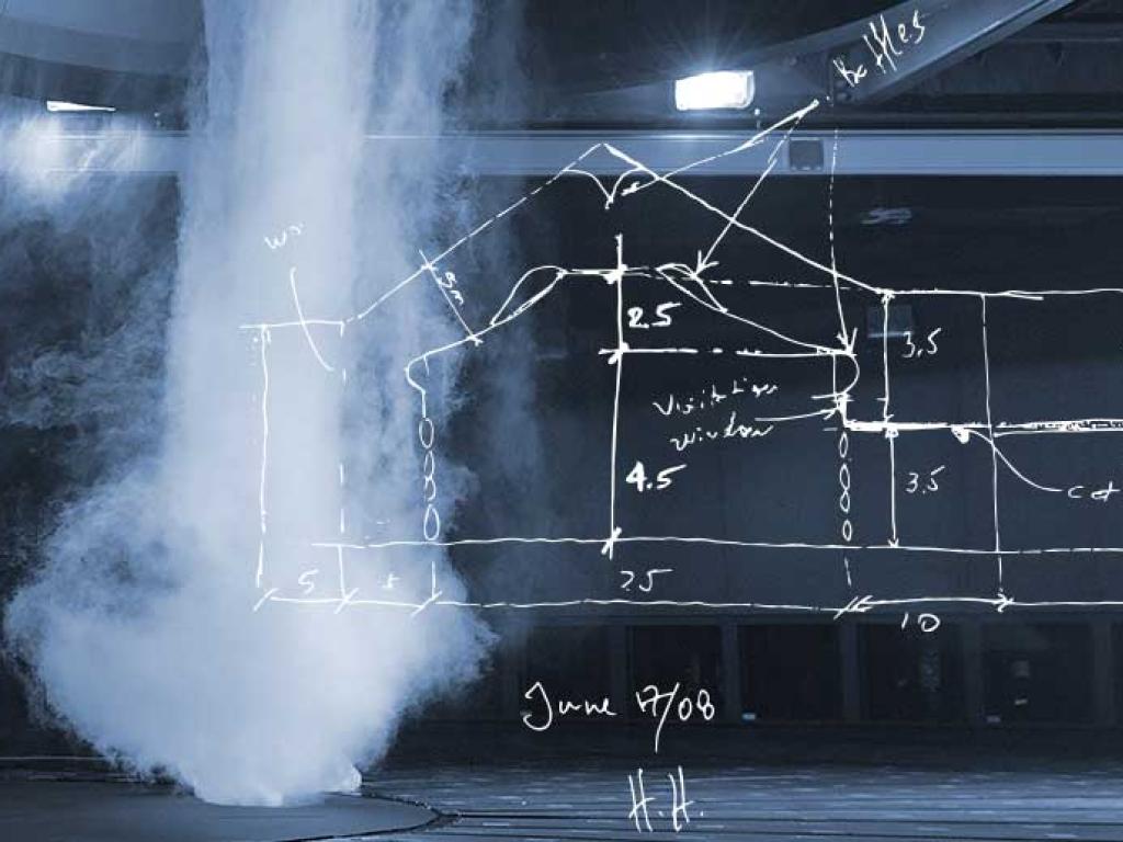 A simulated tornado, looking like a pillar of white mist, rushes up to the ceiling of a large, dark room. A hand-drawn sketch of a wind chamber partially covers the image.