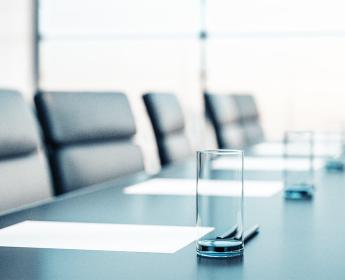 Une table de conférence entourée de chaises vides, sur laquelle se trouvent des verre à eau vides et des feuilles de papier blanches.