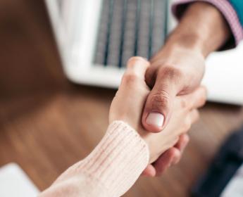 Two people shaking hands over a wooden desk.