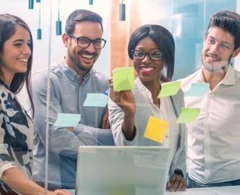 Photo of a group of office employees in front of a glass wall covered in Post-It notes.