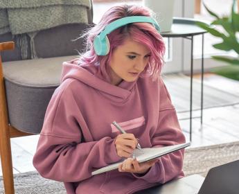 Une jeune personne est assise devant un ordinateur portable tout en prenant des notes sur un cahier.