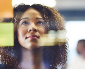 A person in an office looking towards a window with two post-it notes on it. She has a fix and confident look over the shot angle.