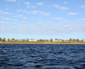 Low buildings and homes along a flat shoreline with water in the foreground. 