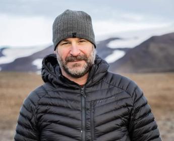 A person wearing a coat in an empty field, posing for a photo.