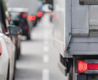 A close-up photo of taillights of a car and a transport truck at the back of a long line of traffic.