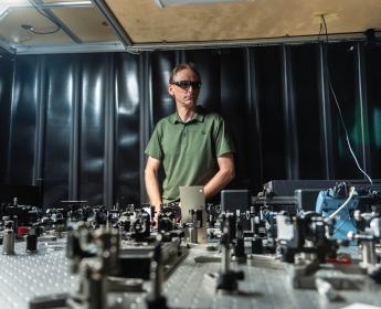 David Jones wears protective laser glasses as he stands behind a prototype on his lab bench.