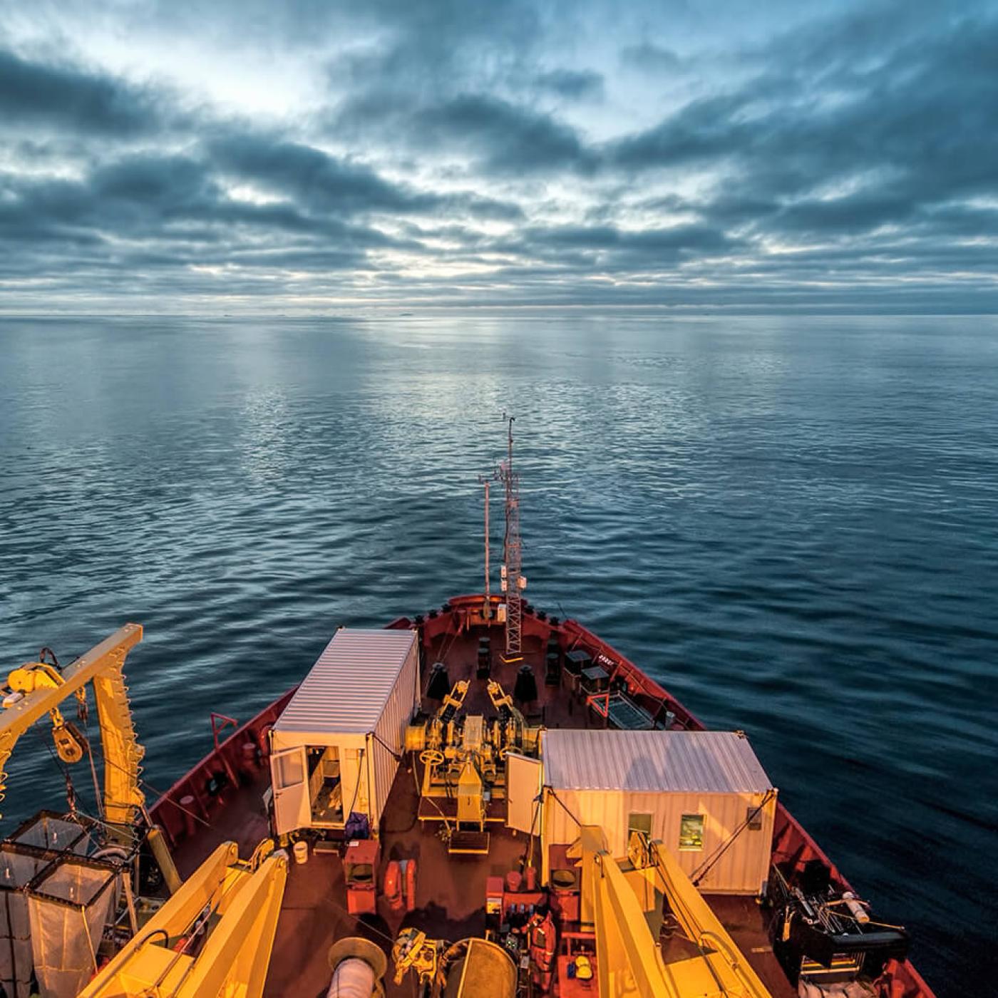 The front of a ship moving through deep water with a dark, cloudy sky