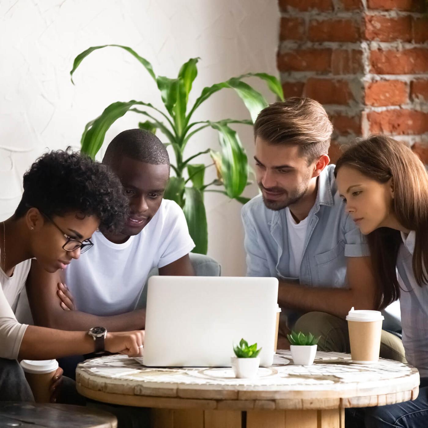 A group of four people in a cafe looking at a laptop.