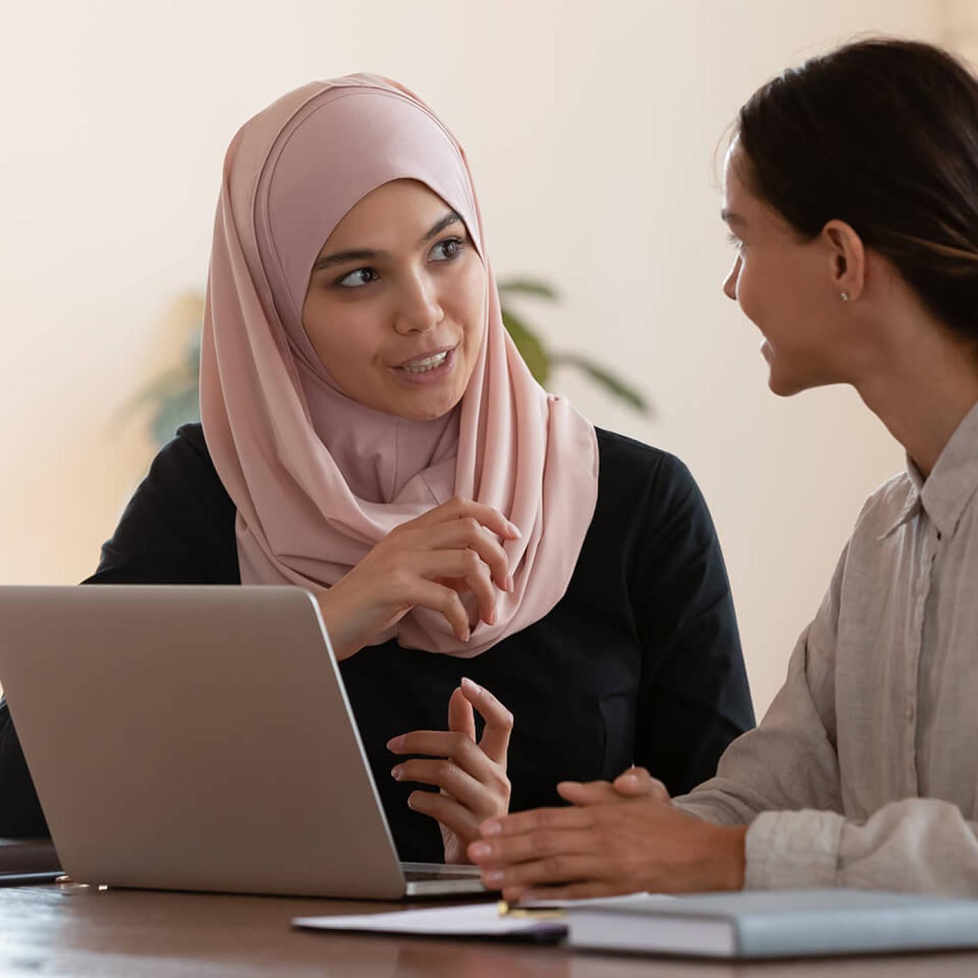 Two people talk in front of a laptop on a wooden table