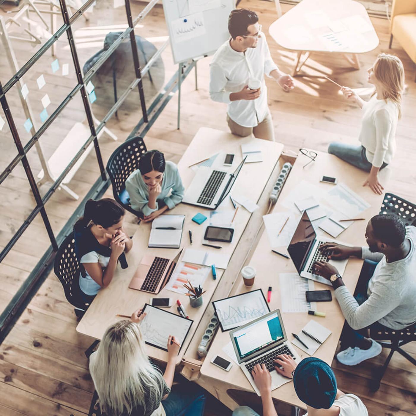 A top-down view of various office employees sitting around a conference table.