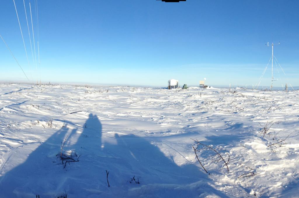 A panorama of a snowy, treeless landscape taken from on top of a snow machine with a meteorological tower and its guy-wires visible.
