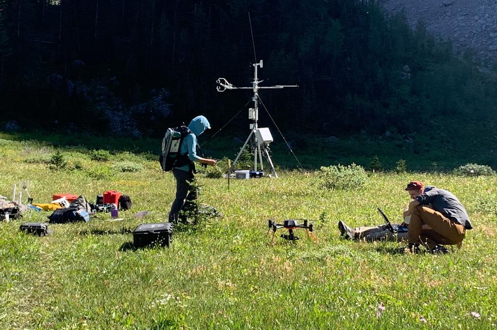 Two people, one standing, one seated in a grassy area with pieces of research equipment around them.